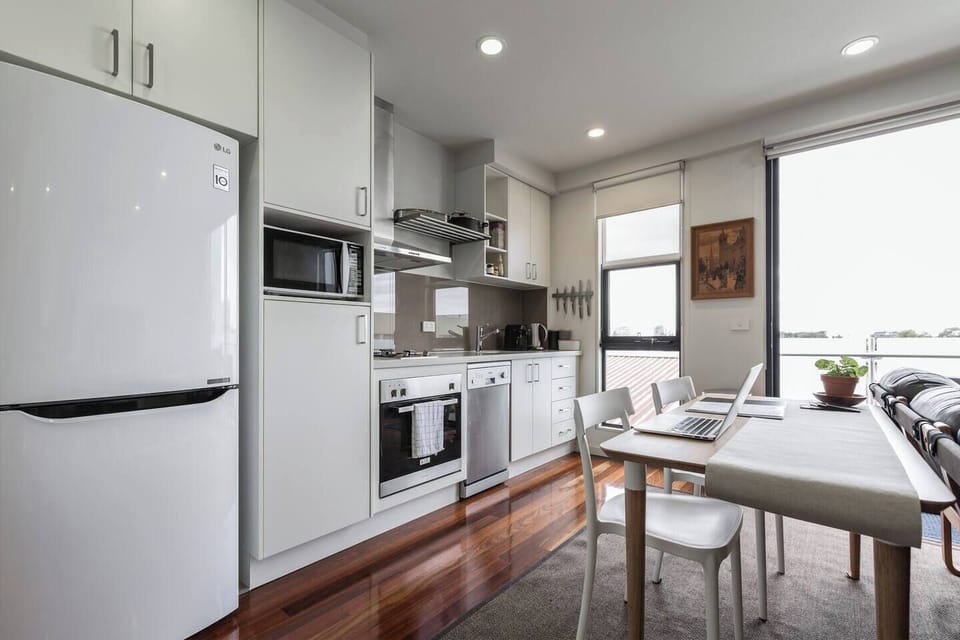 A contemporary kitchen is bright and breezy and sits alongside a dining table that can fit two guests
