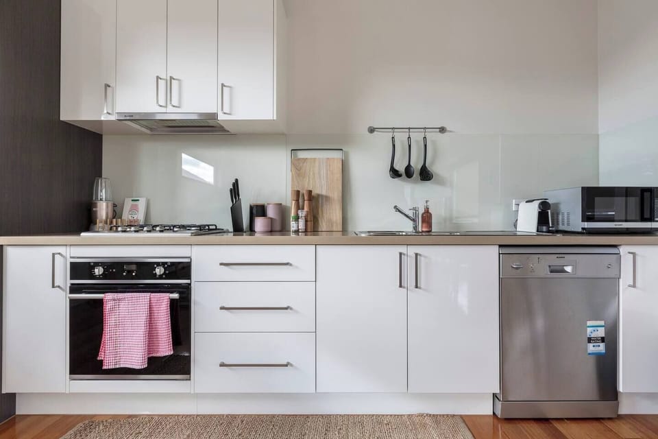 A kitchen has modern appliances including a gas stove, oven, full-sized fridge, microwave, dishwasher as well as added luxuries like a toasted sandwich maker and Nespresso coffee machine
