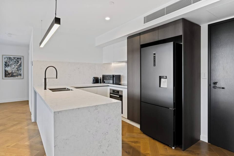 The sleek, open-plan kitchen is designed with stone countertops and high-quality Miele appliances, including an induction cooktop, oven, and dishwasher. 