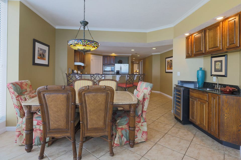 The dining area features a stylish table with wicker chairs, a colorful chandelier, and a wet bar for entertaining