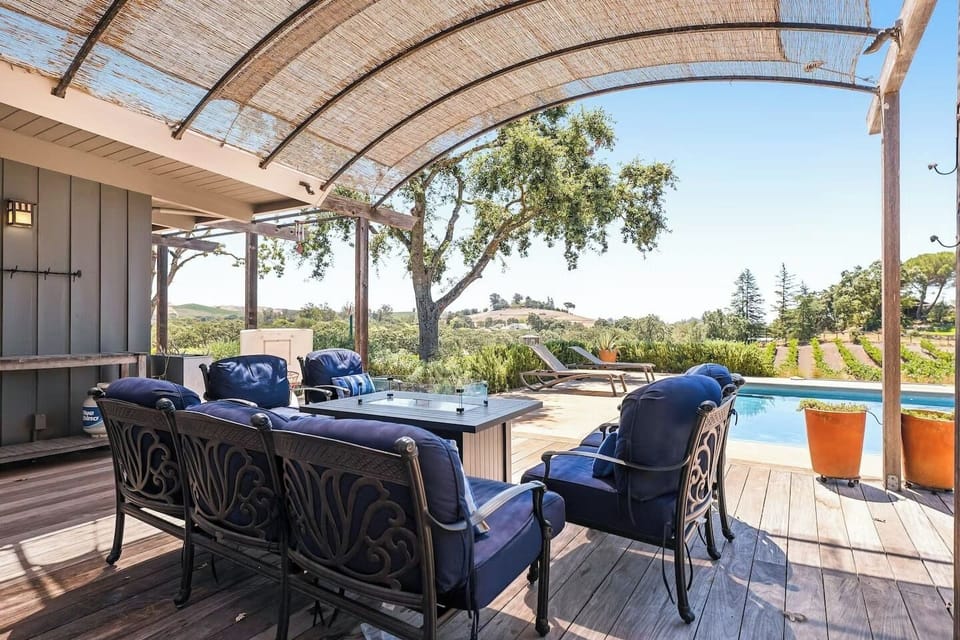 Gorgeous covered poolside lounge with elegant fire pit table, plush blue seating & sweeping vineyard views, the perfect spot for sunset cocktails and long summer evenings. 