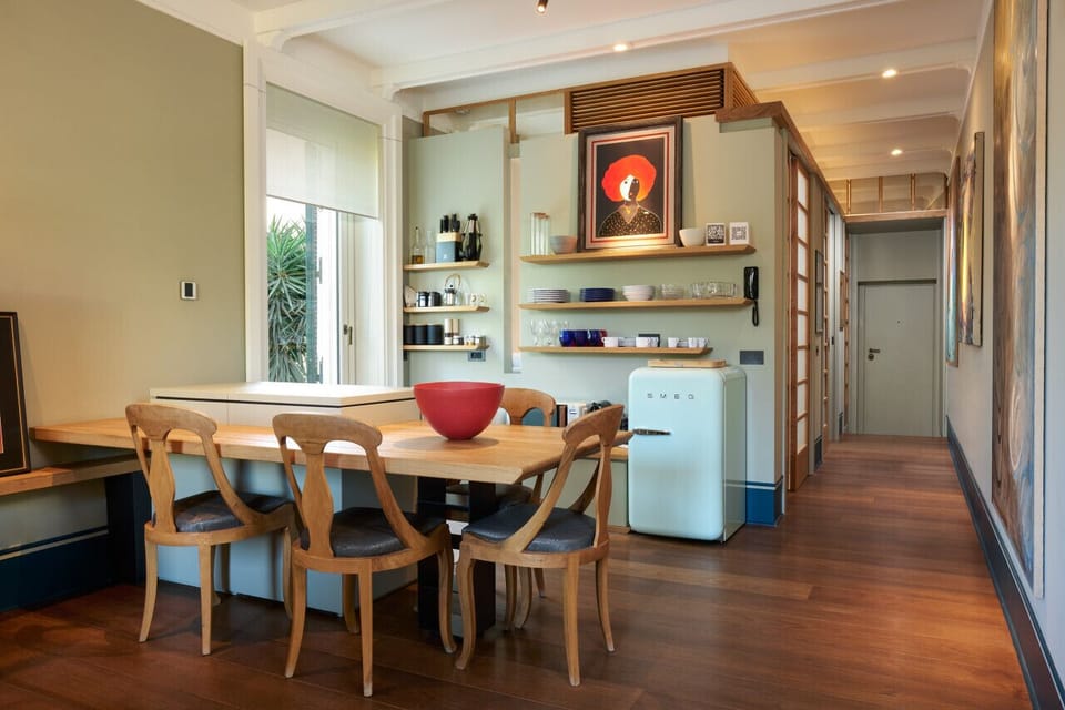 A fully equipped designer kitchen with open shelving and vintage-style appliances opens into a cozy dining space. Warm wood floors and curated art pieces create a stylish yet welcoming atmosphere for shared meals and relaxed moments.
