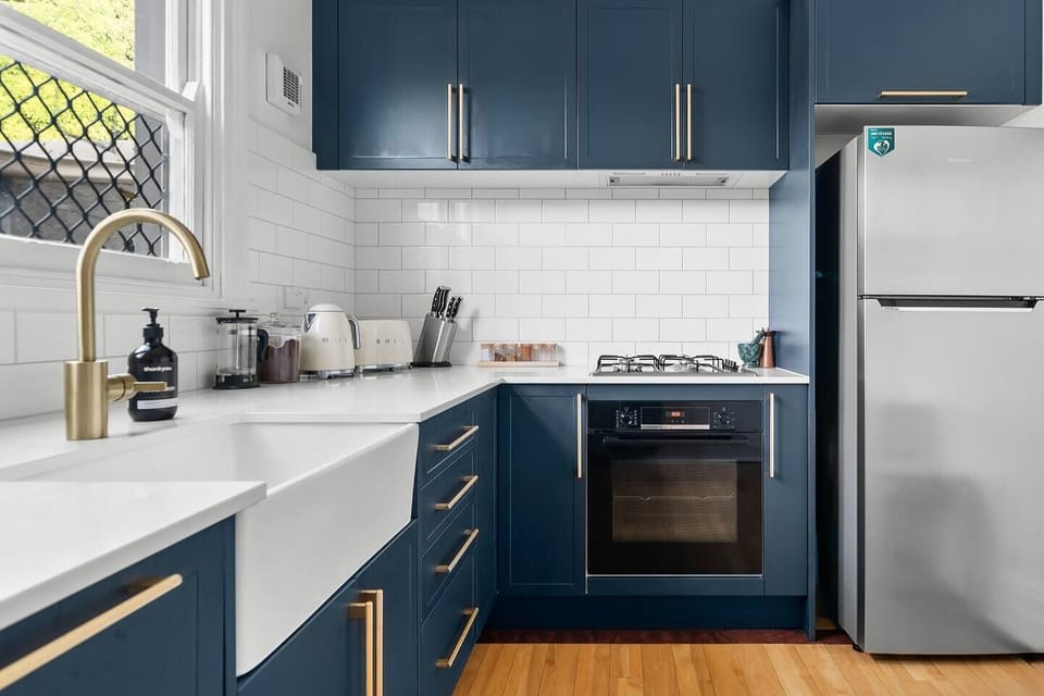 Sleek blue cabinetry, while subway tiles, premium appliances and brushed gold tap ware adorn the well-equipped kitchen.