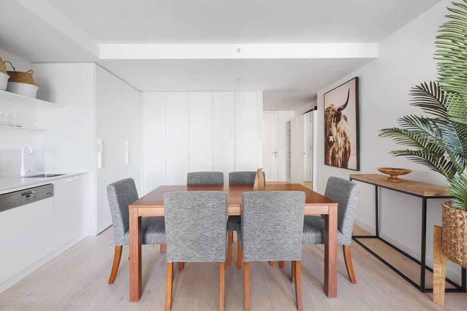The dining area boasts a sturdy wood table with chairs for six people, eclectic artwork and lush house plants