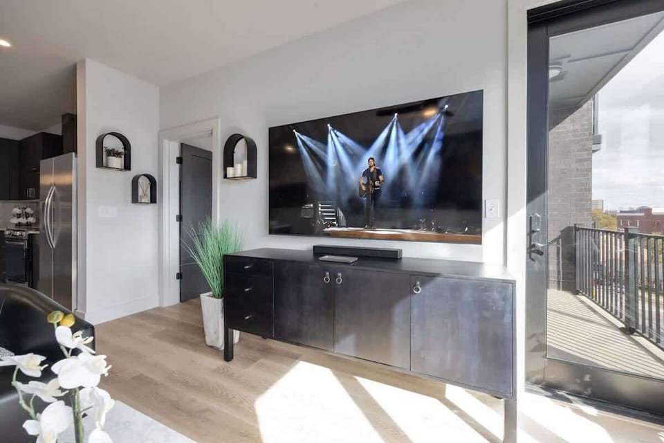 Modern open concept living area with floor to ceiling windows, designer furniture, smart TV, and access to private patio.