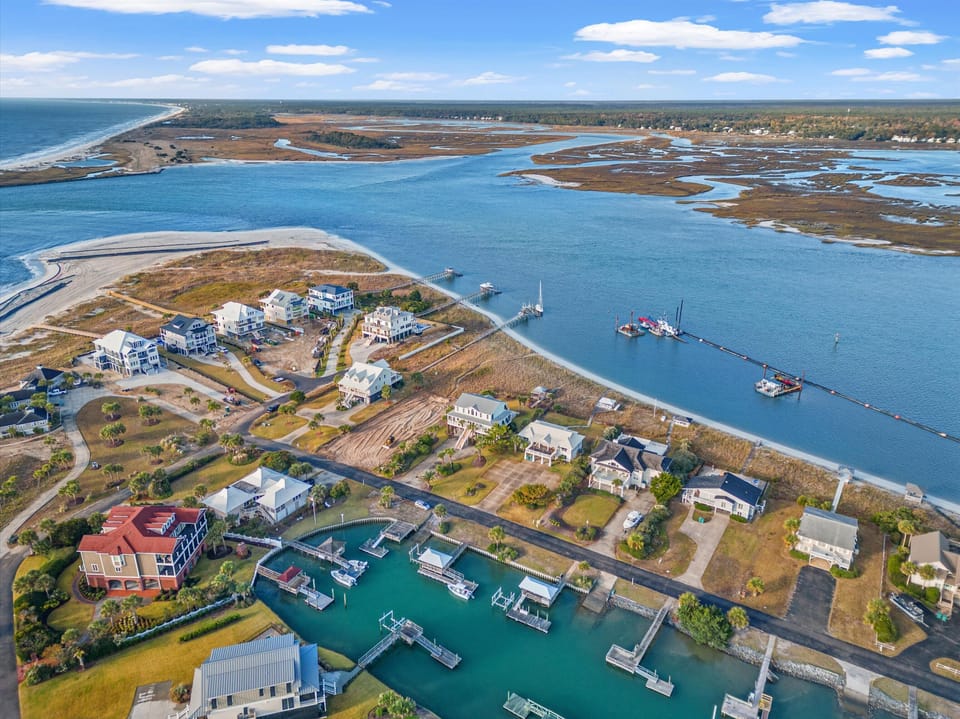 Aerial view of coastal community with waterfront homes, marina, and pristine waters flowing toward the ocean.