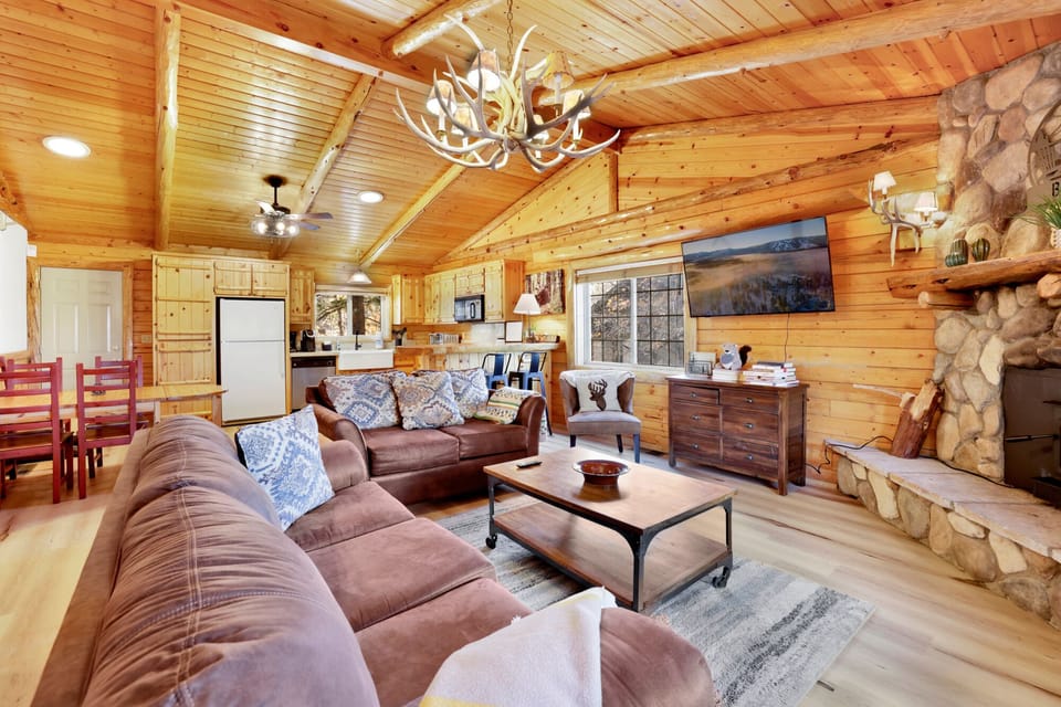 Cozy mountain living room with a stone fireplace, comfy seating, and smart TV—perfect for relaxing evenings, movie nights, and warm cabin vibes after outdoor adventures.
