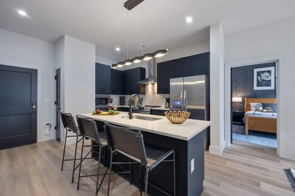 Fully equipped kitchen with stainless steel appliances, basic cooking essentials, toaster, coffee machine, and kitchen island seating.