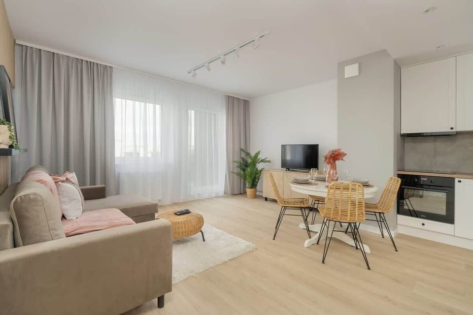 Another angle of the living room, showcasing the comfortable seating area, large windows with sheer curtains, and a flat-screen TV.

