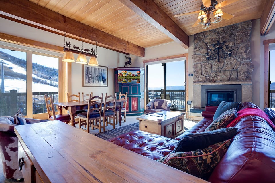 Cozy up by your stone fireplace in this rustic living space with exposed beams and mountain views through every window.