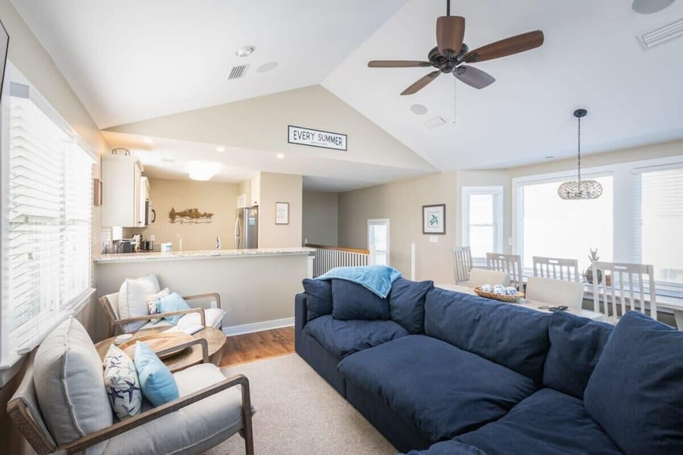 Top Level: Open-concept living area featuring cozy sectional seating, flat-screen TV, expansive windows and sun deck access, plus a convenient bar table with stools.