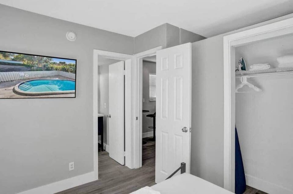 Bedroom doorway with open closet, wood-plank floors, and a glimpse into living area.