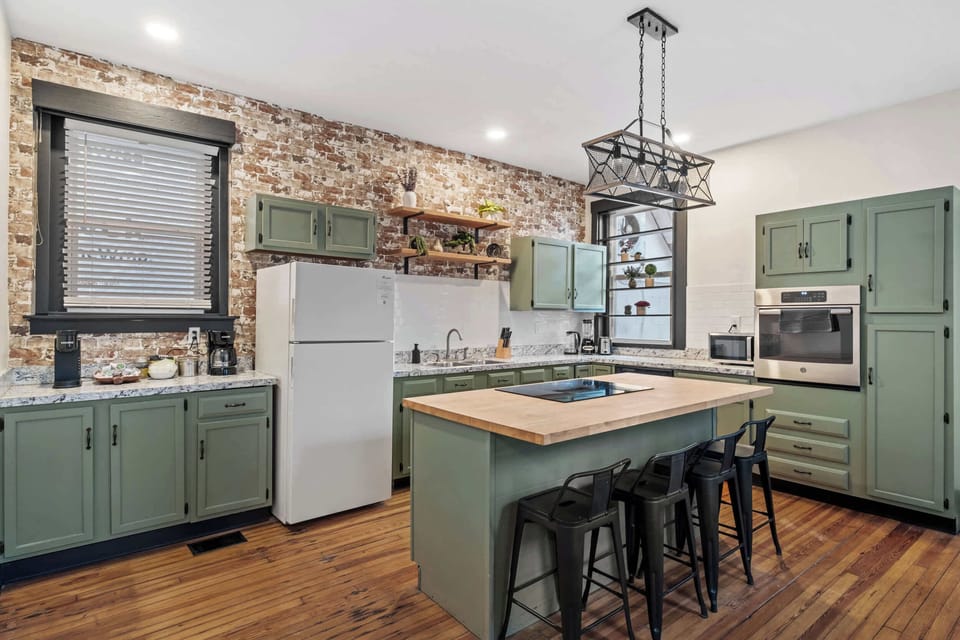 Kitchen: Our kitchen combines modern amenities with rustic charm, featuring a central island for dining and a backdrop of exposed brick.