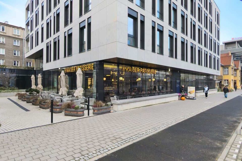 An exterior view of the modern building with a sleek white and black facade, street-level commercial spaces, and a well-maintained pedestrian walkway.







