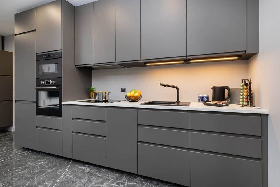 Another view of the all-grey kitchen, highlighting a built-in oven, overhead cabinets, and soft under-cabinet lighting.

