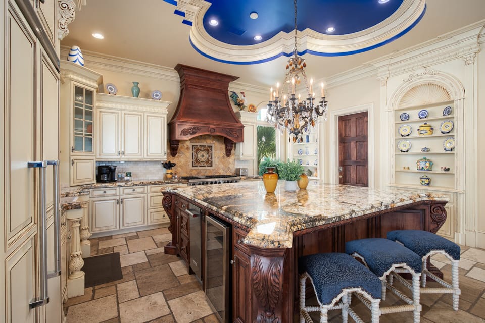 Step into your grand chef's kitchen with ornate details, granite island seating, and stunning blue ceiling that makes cooking feel luxurious.