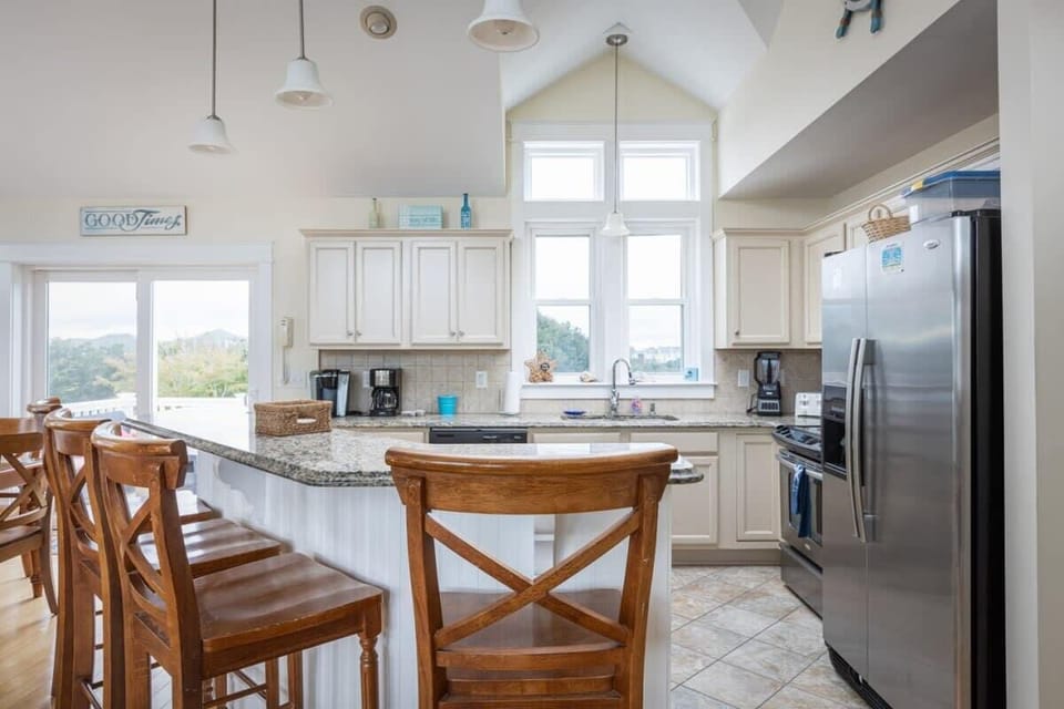 Fully Equipped Kitchen with a Refrigerator, Stove, Oven, Coffee Maker, Breakfast Bar Seating, and Tall Windows that Bring in Natural Daylight.