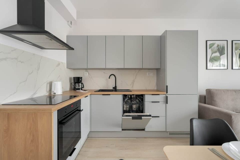 A modern kitchen with grey cabinetry, marble backsplash, and wooden accents, seamlessly connected to the dining area.

