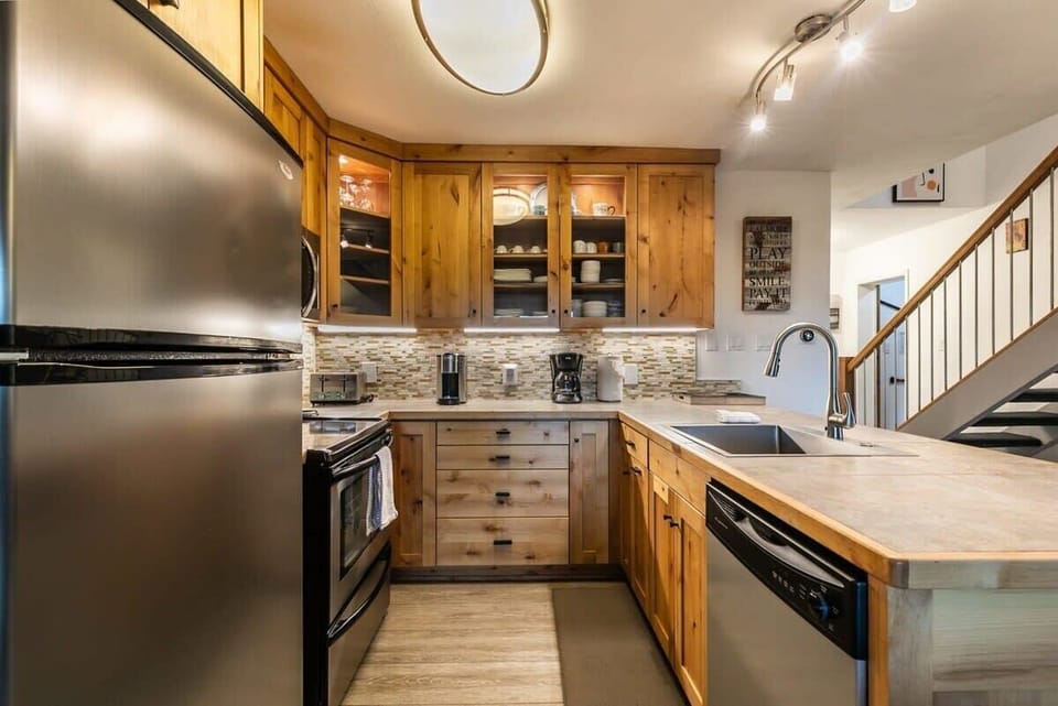 The well-appointed kitchen includes warm wood cabinets, stainless steel appliances, and an expansive kitchen bar adorned with two comfortable bar stools.