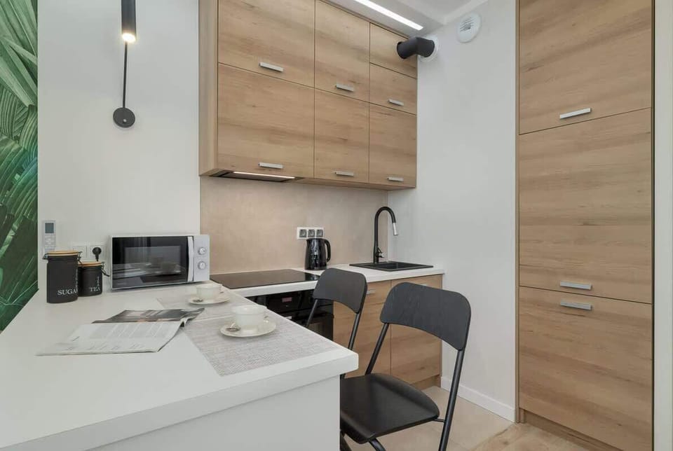 A compact kitchen corner with white cabinets, wooden countertops, and a small dining table for two.

