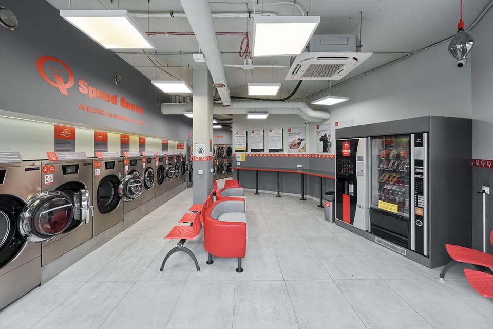 A large, well-lit laundry room with multiple washing machines and dryers. Red seating and vending machines add to the convenience of the space.