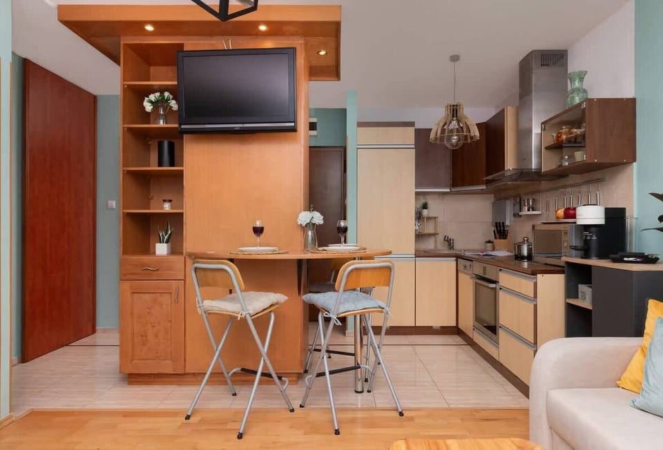 A transitional view between the kitchen and living area, with a small dining table and chairs, and additional storage in wooden cupboards.

