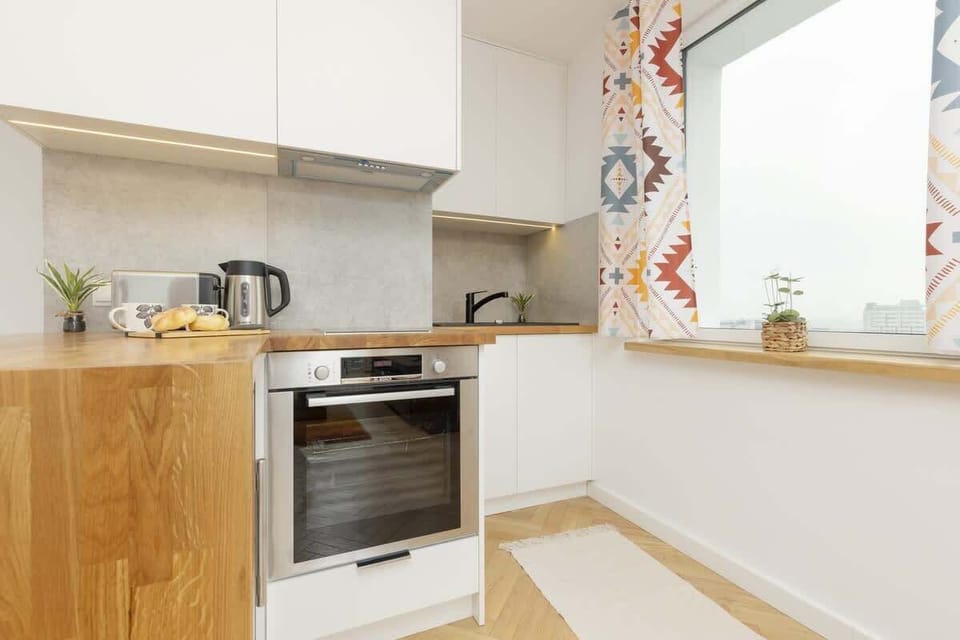A modern kitchen with white cabinets, wooden countertops, and colorful curtains.
