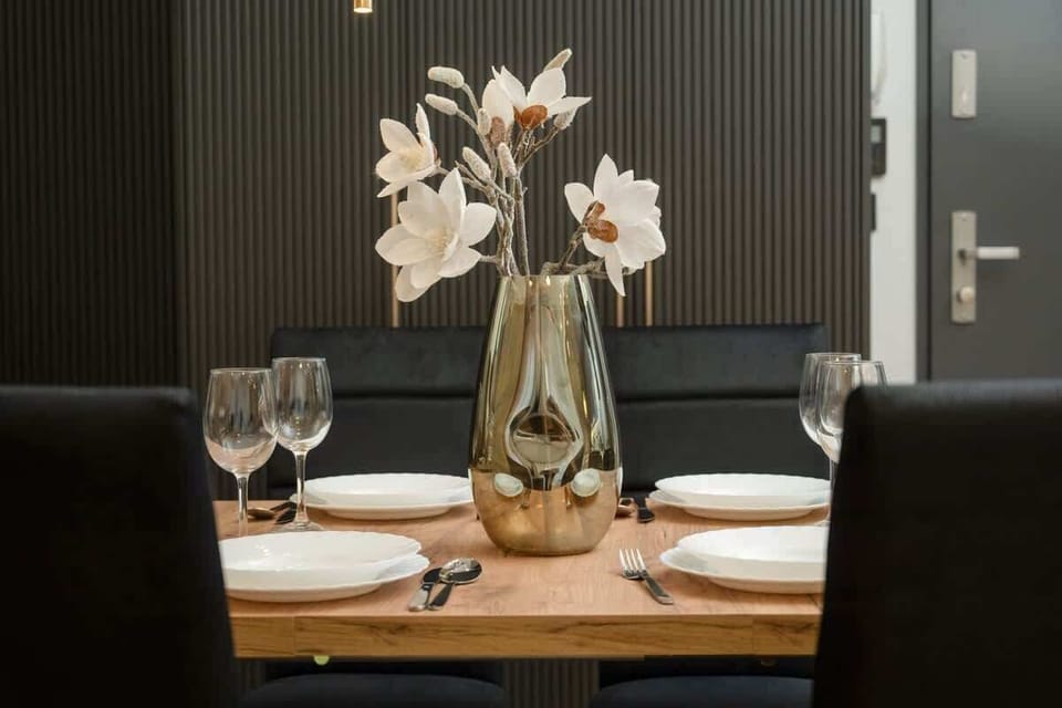 A side view of the dining area featuring a wooden table, blue upholstered chairs, and a decorative gold vase with white flowers.

