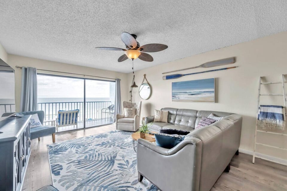 Bright living room w/ coastal decor, ceiling fan, and sliding doors to the balcony.