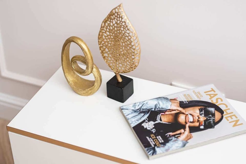 A white side table adorned with a gold abstract sculpture, a glossy magazine, and a small accent piece for a stylish decorative detail.

