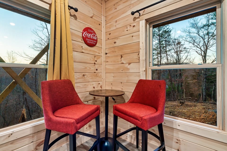 Inviting corner featuring red bar-height chairs, a Coca-Cola sign, and scenic woodland views.