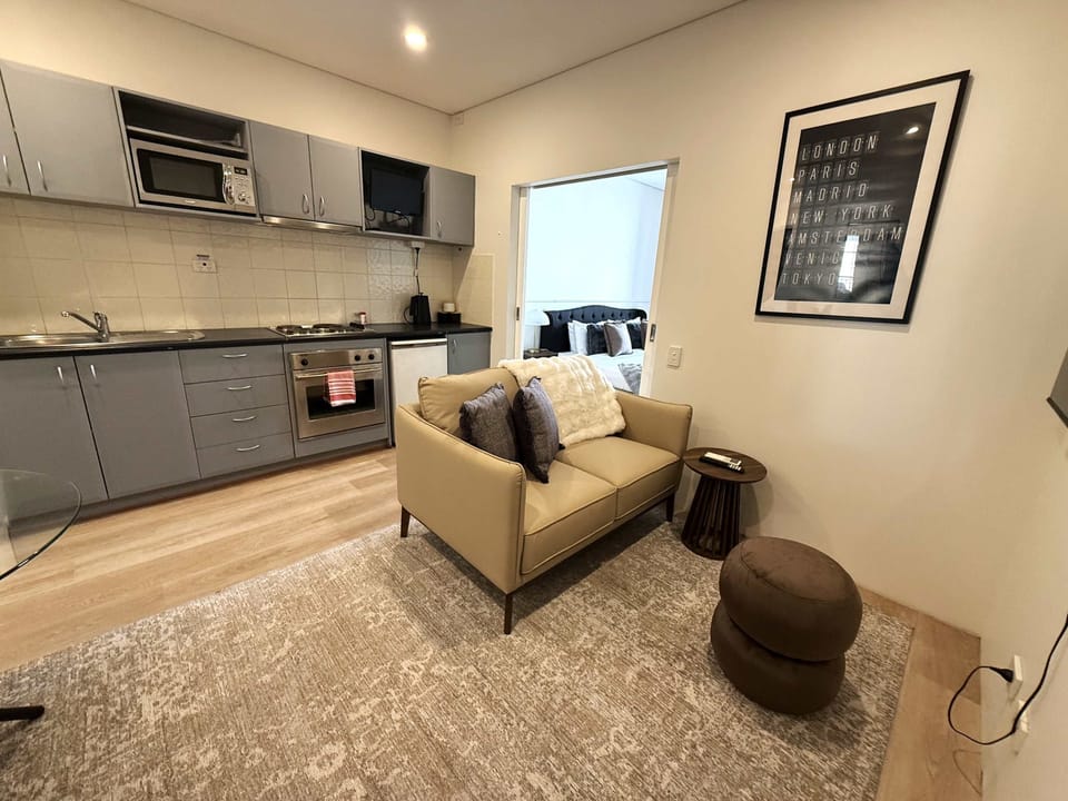 Unwind in this contemporary studio featuring a comfortable sofa, Smart TV, and a fully equipped kitchenette with a cooktop, oven, microwave, and fridge. A welcoming space that combines modern comfort with everyday convenience for a memorable stay.