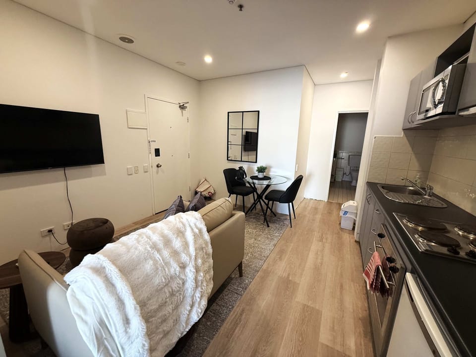 Enjoy a modern open-plan retreat featuring a comfortable sofa, Smart TV, dining table for two, and a fully equipped kitchenette with a cooktop, oven, microwave, and fridge. Stylish, functional, and designed for a relaxing and convenient stay.