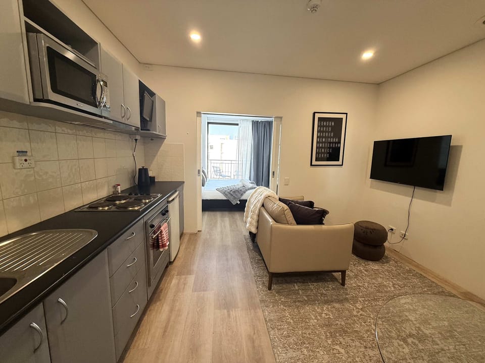 Relax in this modern open-plan retreat featuring a cozy sofa, Smart TV, and a fully equipped kitchenette with a cooktop, oven, microwave, kettle, and fridge. Perfect for unwinding, preparing meals, and enjoying a hassle-free stay.