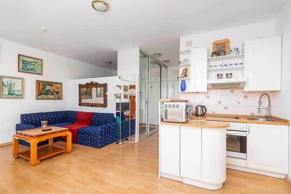 An open-plan living space revealing a simple kitchen corner, white cabinetry, and a blue sofa, with more artwork displayed on the walls.

