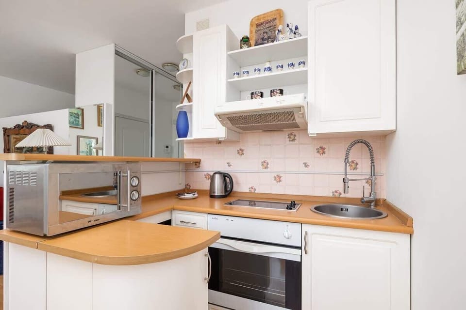 A compact white kitchen with a wooden countertop, decorative backsplash, microwave, and open shelving for added storage.

