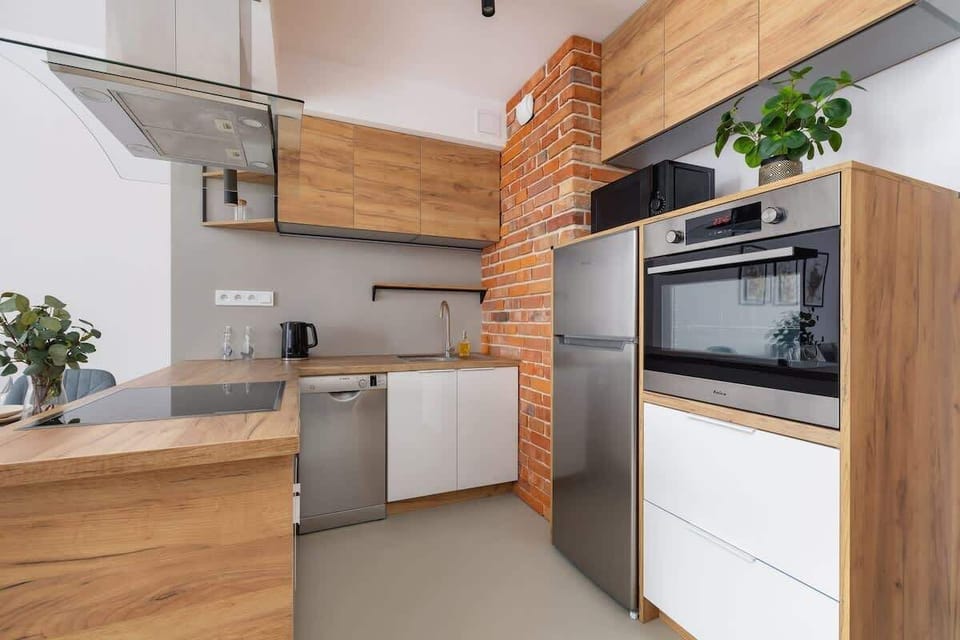 An open kitchen with wooden cabinetry, exposed brick accents, and built-in stainless steel appliances for a rustic yet modern style.

