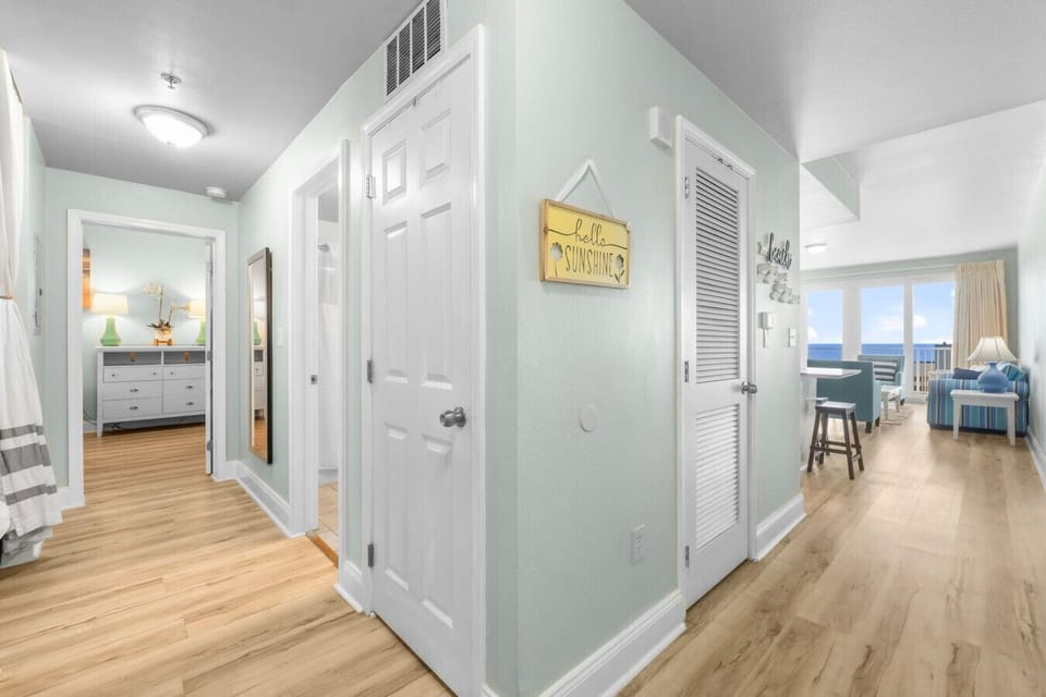 Bright hallway with coastal decor and light wood flooring leads to a charming living area with stunning ocean views and a second bedroom