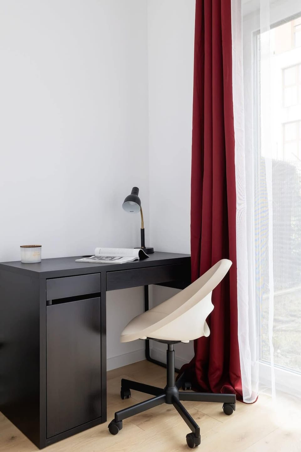 A small workspace with a sleek black desk, modern white chair, and bright red curtains, creating a functional and stylish office nook.
