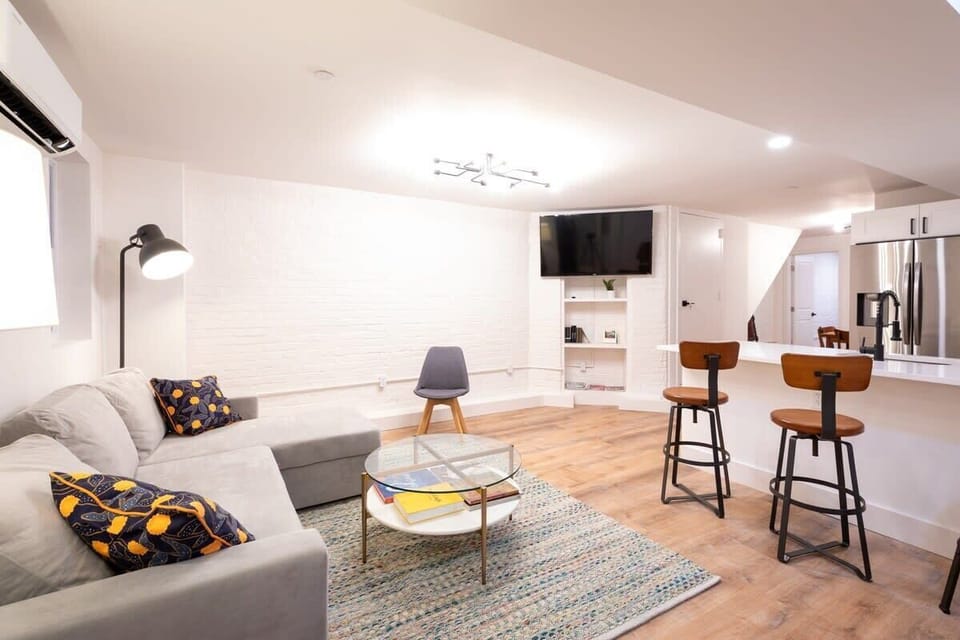 Queen size sleeper sofa with an area rug, coffee table, bar stools at the counter and a wall mounted tv above built in storage. 