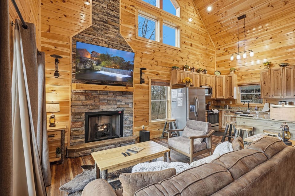 Your cozy cabin retreat features warm wood walls, stone fireplace, and open kitchen—perfect for unwinding after mountain adventures.