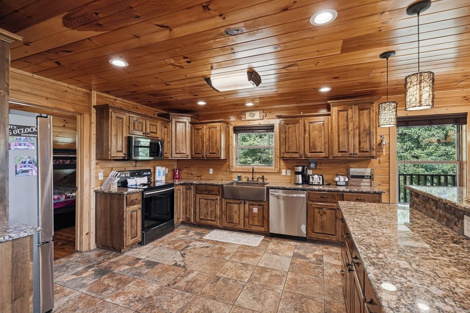 Your spacious gourmet kitchen features warm wood cabinetry, granite countertops, stainless appliances, and a farmhouse sink—perfect for preparing meals while enjoying views of lush greenery through expansive windows.