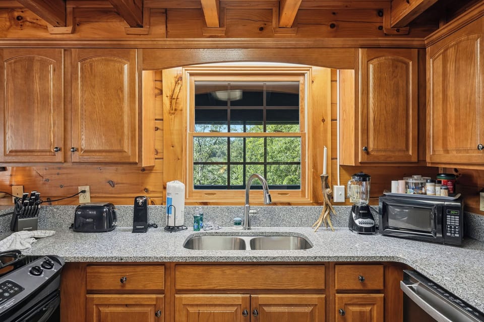 Your fully equipped kitchen features granite countertops, rich wood cabinetry, and a window overlooking peaceful greenery—perfect for preparing meals in rustic elegance.