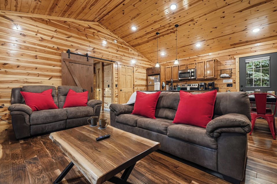 Unwind in this beautifully crafted cabin with warm wood tones throughout. Sink into plush seating adorned with bright red pillows, while the rustic barn door and handcrafted coffee table add charming character to your stay.