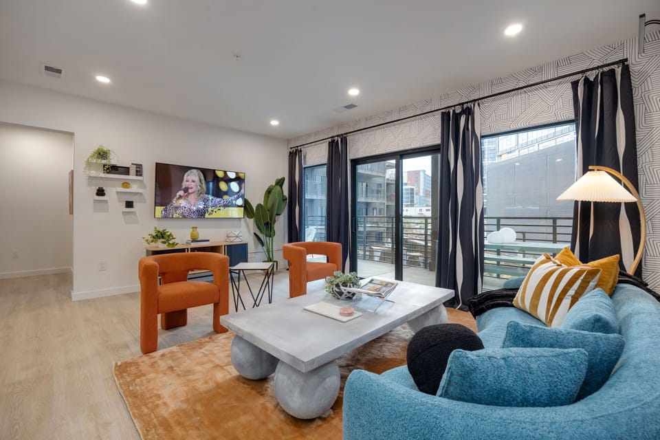 Bright open living space featuring SMART flat-screen TV, designer furnishings, and patio entrance with pool view.