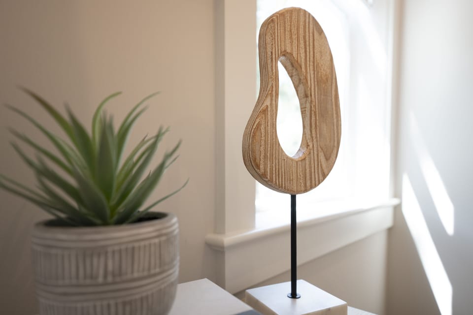 Wood oval art in front of a bright window.