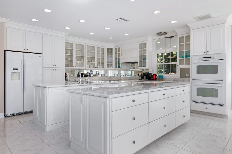 Large white kitchen with boasting two islands, sleek white fridge, double oven, and stove