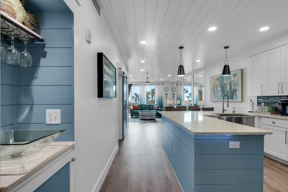Your spacious kitchen flows into the living area, featuring sleek blue cabinets, marble countertops, and modern pendant lighting.