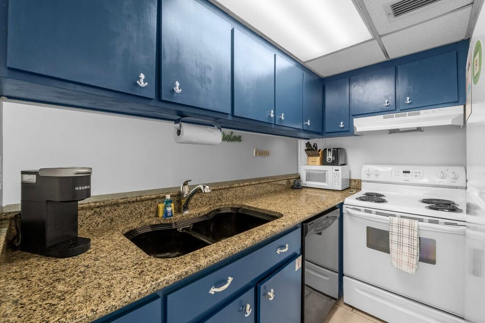 Fully equipped kitchen features granite countertops, navy cabinetry with coastal charm, and modern appliances, including a Keurig and microwave, for all your cooking needs