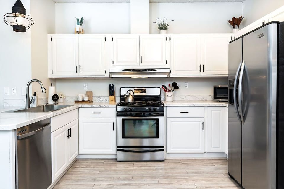 Sleek white kitchen w/ stainless steel appliances & ample counter space for cooking.